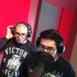 a front view of two vocalists recording their tracks in front of a shure 7b microphone with pop filter in front of it.