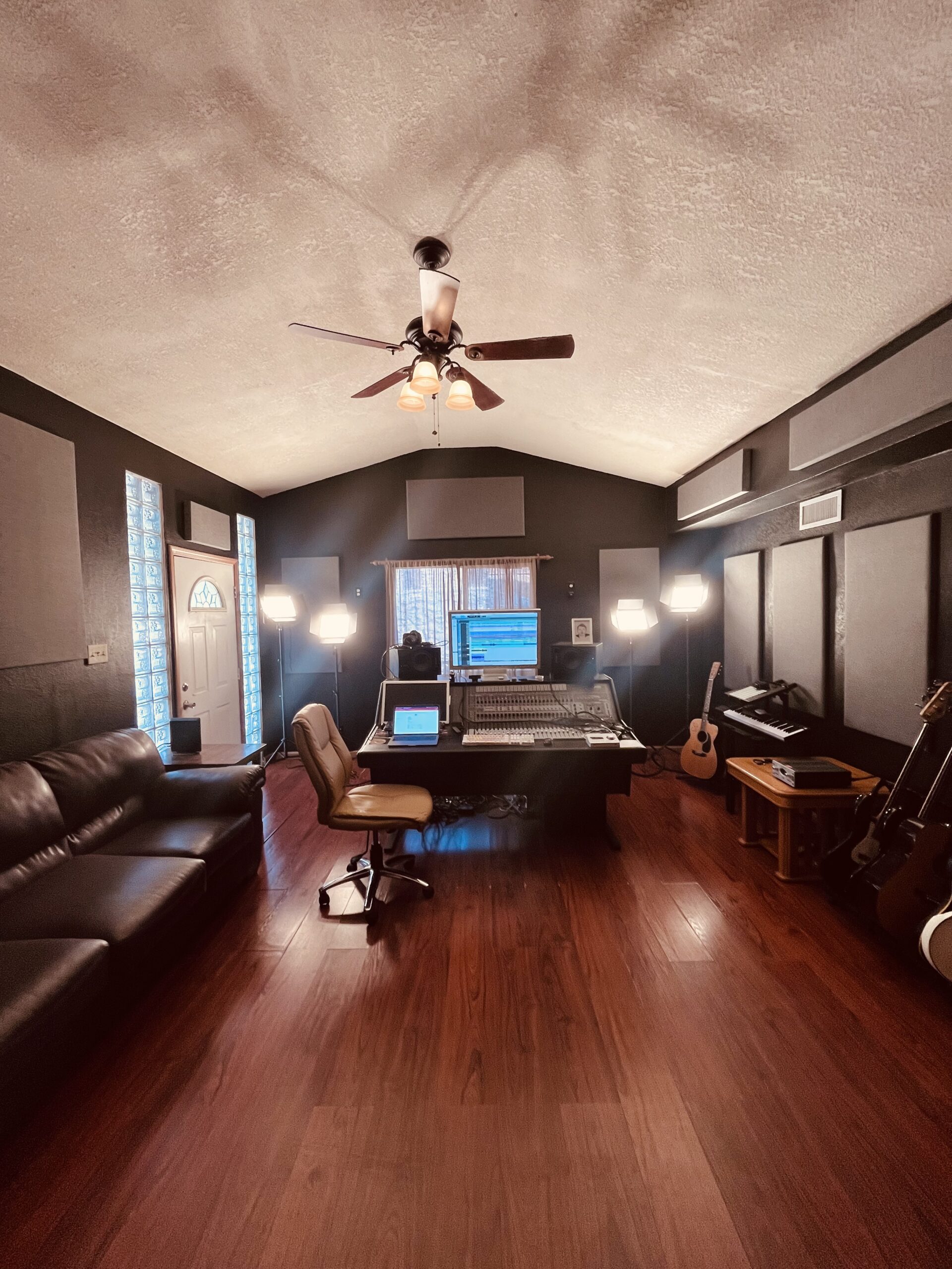 A front view of the control room at let down studio with a leather couch, leather rolling chair and mixing board with 4 white lights illuminating the room.