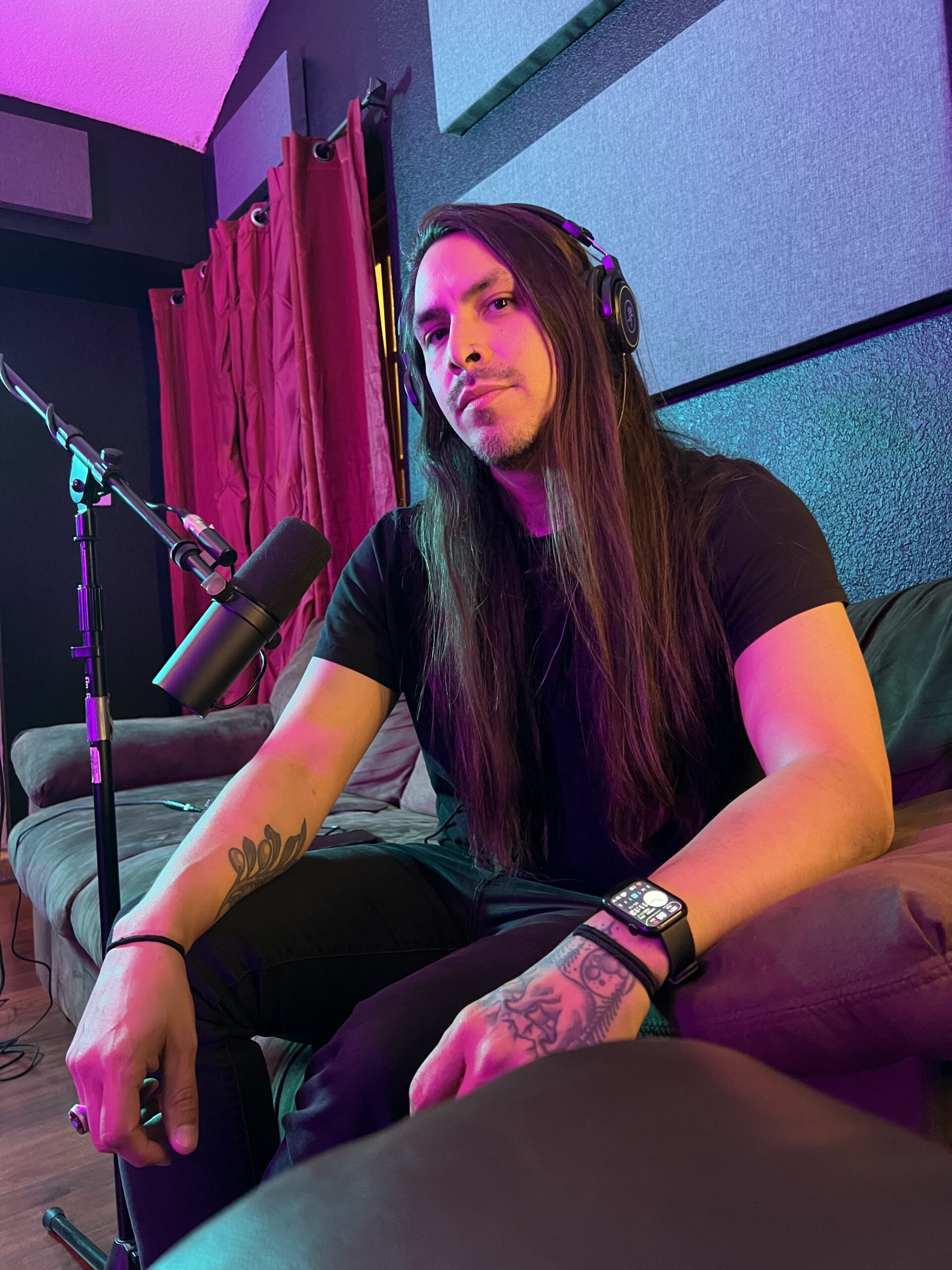 A front view of Leo Olivas wearing headphones in front of a shrure 7b microphone sitting on a couch.